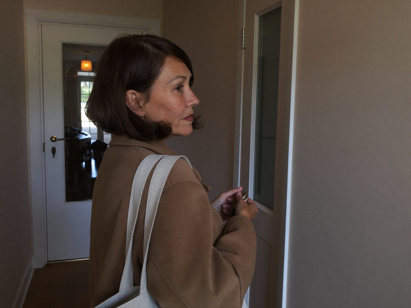 Vrouw in jas staat vroeg in de ochtend in de gang en kijkt naar de voordeur, klaar om te vertrekken